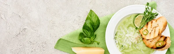Tiro panorâmico de deliciosa sopa de legumes verde cremoso com croutons servidos em guardanapo perto de folhas de espinafre e queijo — Fotografia de Stock