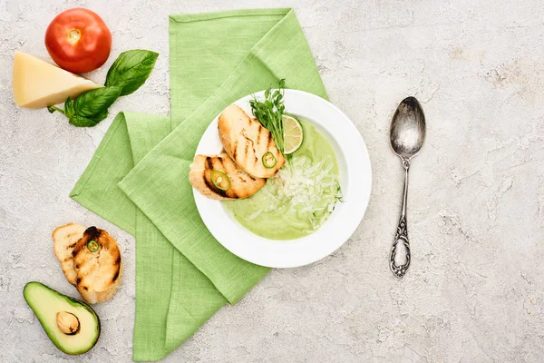 Вид на вкусный сливочно-зеленый суп с гренками рядом со свежими ингредиентами — стоковое фото