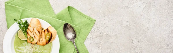 Panoramic shot of delicious creamy green vegetable soup with sprouts and croutons served with napkin and spoon — Stock Photo