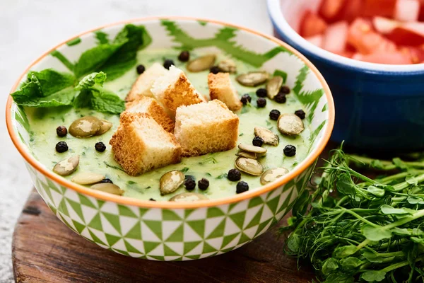 Bowl of delicious green vegetable creamy soup with croutons, black pepper and pumpkin seeds — Stock Photo