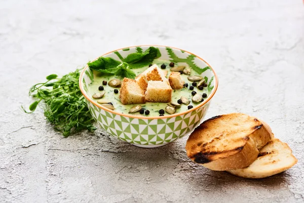 Миска вкусного зеленого овощного сливочного супа с гренками, ростками, черным перцем и тыквенными семечками — стоковое фото