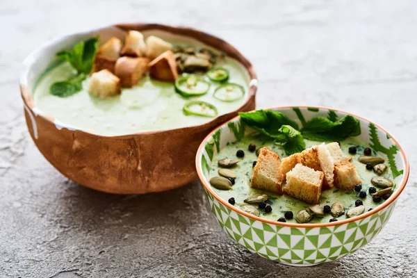 Ciotole di gustosa zuppa di verdure verdi cremose con crostini, jalapenos, pepe nero e semi di zucca — Foto stock