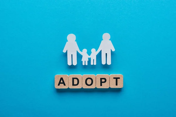 Top view of paper cut gay family holding hands on blue background with adopt lettering on wooden cubes — Stock Photo