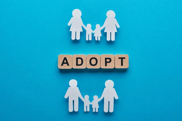 Top view of paper cut gay and lesbian families holding hands on blue background with adopt lettering on wooden cubes — Stock Photo