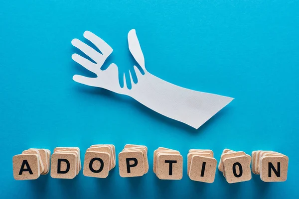 Top view of paper cut parent and child hands and adoption lettering on blue background — Stock Photo