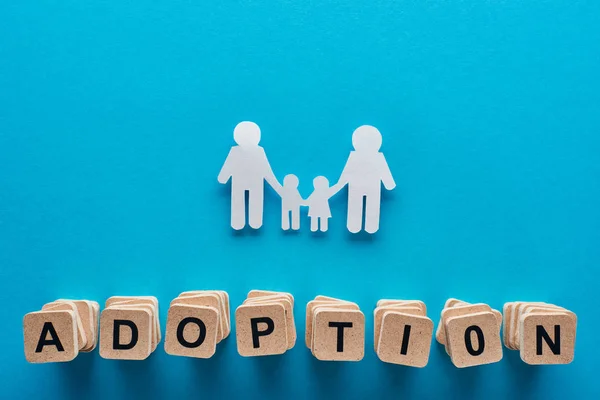 Top view of paper cut gay family holding hands on blue background with adoption lettering on wooden cubes — Stock Photo