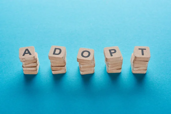 Wooden blocks with adopt lettering on blue background — Stock Photo