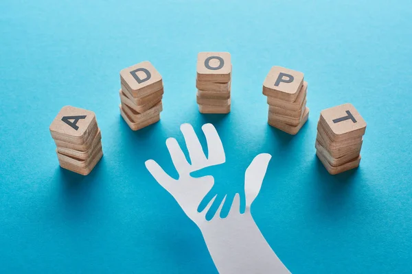 Wooden blocks with adopt lettering near paper cut parent and child hands on blue background — Stock Photo