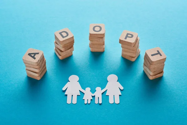 Wooden blocks with adopt lettering near paper cut lesbian family on blue background — Stock Photo