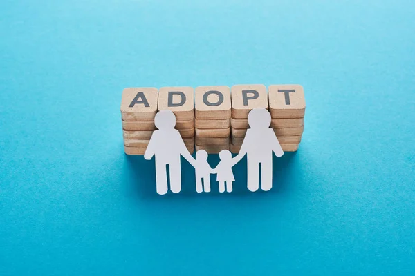 Wooden blocks with adopt lettering near paper cut gay family on blue background — Stock Photo