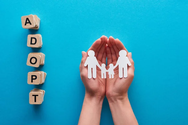 Ritagliato vista di donna in possesso di carta tagliato gay famiglia vicino blocchi con adottare lettering su sfondo blu — Foto stock