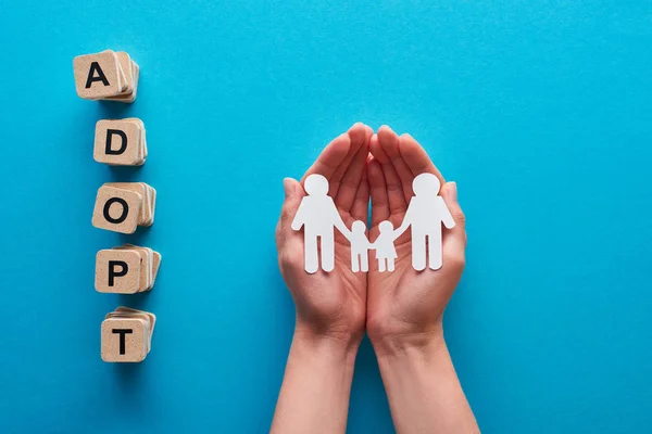 Recortado vista de la mujer sosteniendo papel corte gay familia cerca de bloques con adoptar letras sobre fondo azul - foto de stock