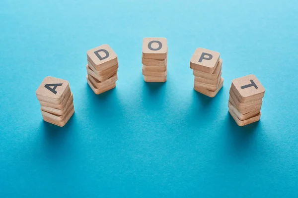 Wooden blocks with adopt lettering on blue background with copy space — Stock Photo