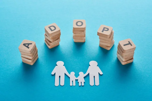 Holzblöcke mit Adoptiv-Schriftzug in der Nähe einer papiergeschnittenen schwulen Familie auf blauem Hintergrund — Stockfoto