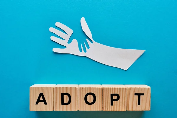 Top view of paper cut parent and child hands and adopt lettering on blue background — Stock Photo