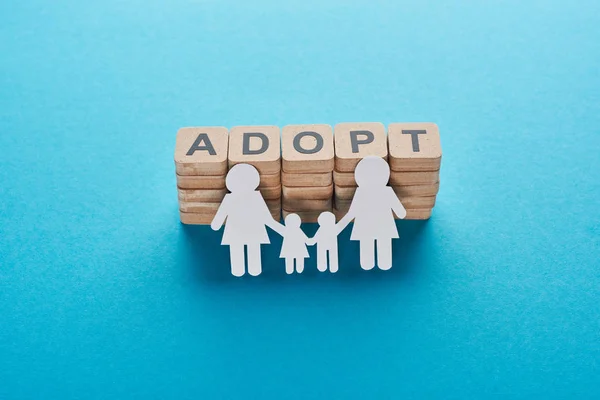 Paper cut lesbian family holding hands on blue background with adopt lettering on wooden cubes — Stock Photo