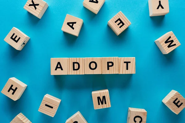 Top view of adopt word made of wooden cubes on blue background — Stock Photo