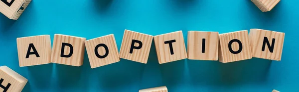 Top view of adoption word made of wooden cubes on blue background, panoramic shot — Stock Photo