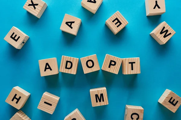 Top view of adopt word made of wooden cubes on blue background — Stock Photo