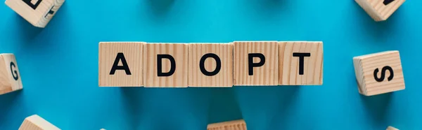 Top view of adopt word made of wooden cubes on blue background, panoramic shot — Stock Photo