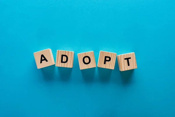 Top view of adopt word made of wooden cubes on blue background — Stock Photo