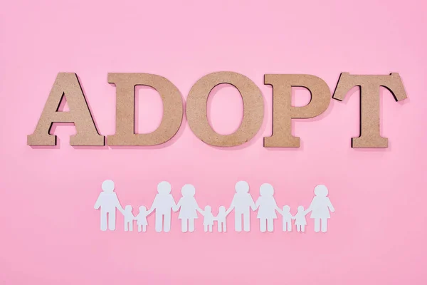 Top view of cardboard word adopt and paper cut families on pink background — Stock Photo