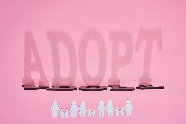 Ombre de mot adopter et couper le papier familles sur fond rose — Photo de stock
