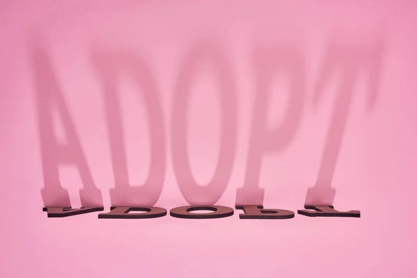 Ombre de mot adopter sur fond rose — Photo de stock