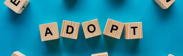 Top view of adopt word made of wooden cubes on blue background, panoramic shot — Stock Photo