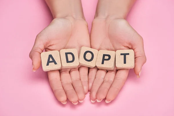 Cropped view of woman holding cubes with adopt lettering on pink background — Stock Photo