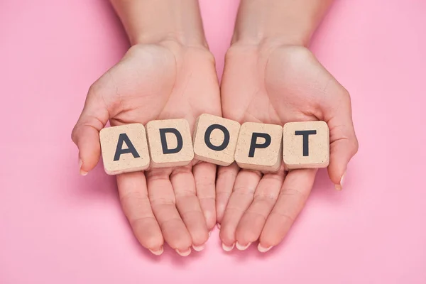 Vista ritagliata di donna che tiene cubi con adottare lettering su sfondo rosa — Foto stock