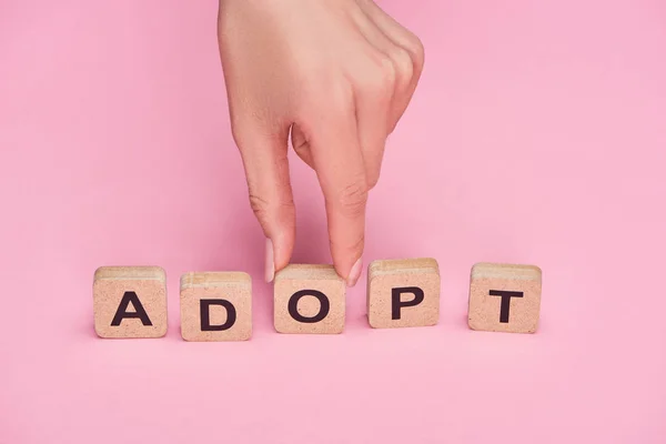 Cropped view of female hand near cubes with adopt lettering on pink background — Stock Photo