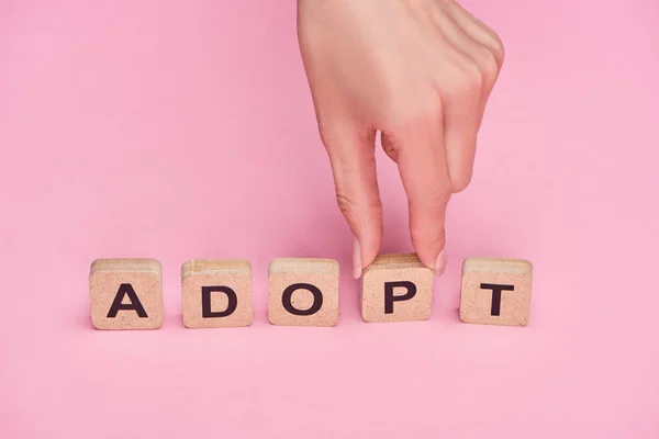 Partial view of female hand near cubes with adopt lettering on pink background — Stock Photo