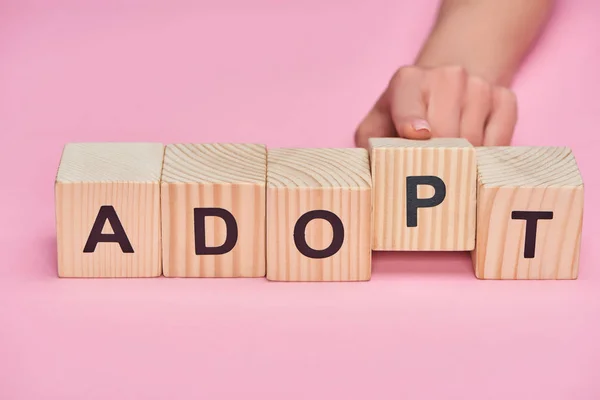 Cropped view of female hand near wooden cubes with adopt lettering on pink background — Stock Photo