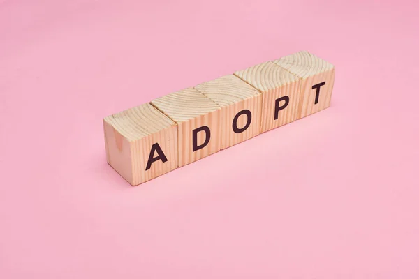 Cubos de madeira com adotar letras no fundo rosa — Fotografia de Stock