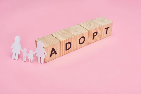 Wooden cubes with adopt lettering and paper cut lesbian family on pink background — Stock Photo