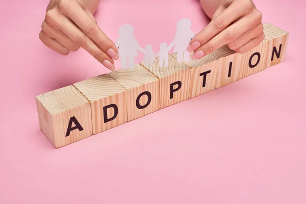 Cropped view of woman holding paper cut lesbian family on wooden cubes with adoption lettering on pink background — Stock Photo