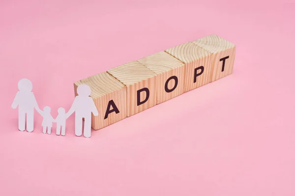 Wooden cubes with adopt lettering and paper cut gay family on pink background — Stock Photo