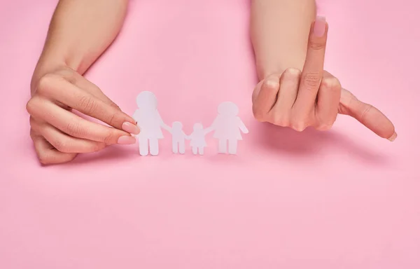 Cropped view of woman holding paper cut lesbian family and showing middle finger on pink background — Stock Photo