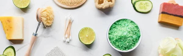 Panoramic shot of bath salts, body brush and ear sticks near natural soap and fresh cucumber and lime pieces on marble surface — Stock Photo