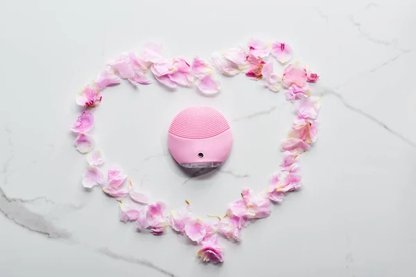 Vista dall'alto di silicone pulizia del viso spazzola petali rosa sulla superficie di marmo — Foto stock