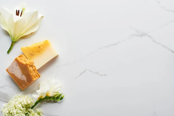 Vue de dessus des morceaux de savon naturel près des fleurs fraîches sur la surface du marbre — Photo de stock