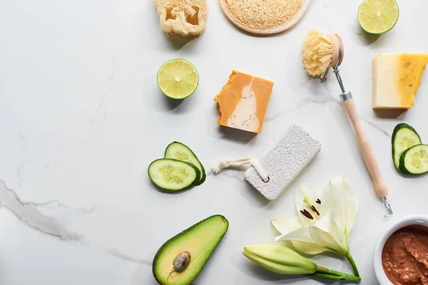 Top view of natural soap pieces, body brush, loofah and pumice stone near fresh flower, lime, cucumber and avocado on marble surface — Stock Photo