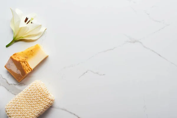 Vista superior de jabón natural cerca de esponja de baño y flor fresca en la superficie de mármol - foto de stock