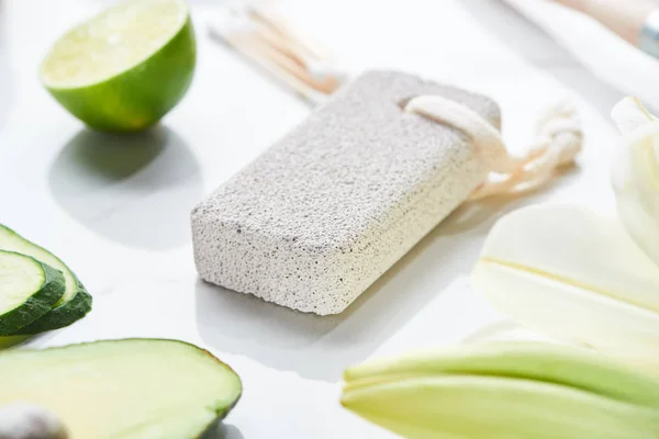 Close up view of gray pumice stone near fresh lime and cucumber on white surface — Stock Photo