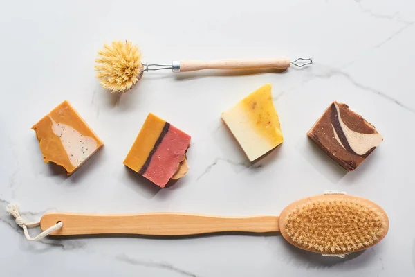 Vue de dessus des morceaux de savon faits maison et des brosses pour le corps sur la surface du marbre — Photo de stock