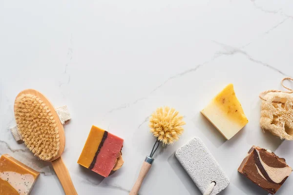 Top view of homemade soap pieces, pumice stone and body brushes on marble surface — Stock Photo