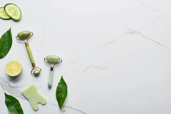 Vista superior de la espátula, rodillos de masaje, hojas verdes frescas, rodajas de cal y pepino en la superficie de mármol - foto de stock