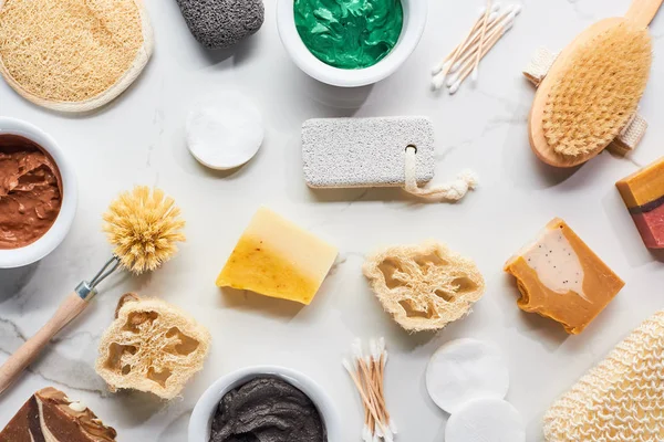 Vista superior de esponjas de baño, cepillos para el cuerpo, artículos de higiene, jabón y máscara de arcilla en la superficie de mármol - foto de stock