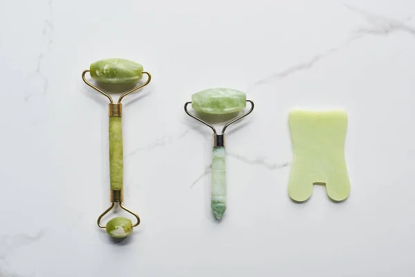 Top view of jadeite facial rollers and spatula on marble surface — Stock Photo